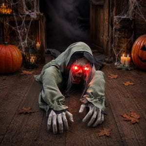 A creepy Halloween decoration of a hooded zombie or ghost crawling forward on a wooden floor, with glowing red eyes and pale hands. The scene is styled for Halloween with pumpkins, candles, cobwebs, and autumn leaves.
