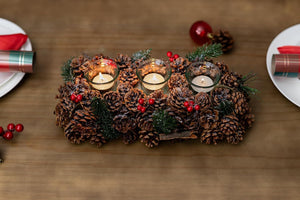 Decorative centerpiece made of pine cones and candles on a wooden table.