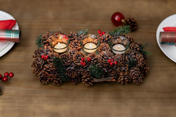 Decorative centerpiece made of pine cones and candles on a wooden table.