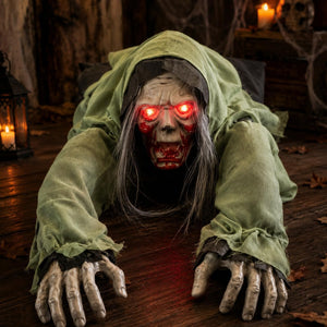 A creepy Halloween decoration of a crawling zombie witch in a tattered green hood, with glowing red LED eyes and skeletal hands, crawling on a wooden floor.