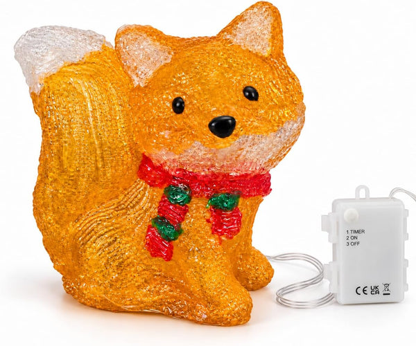 A glittery orange fox-shaped LED night light with a red and green scarf, shown next to its white power adapter on a white background.