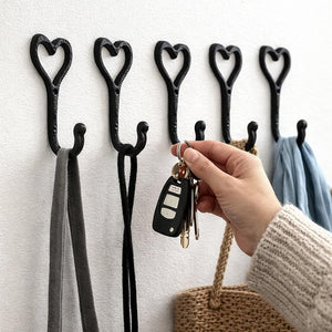 Heart-shaped hooks on a wall with a hand holding keys and a purse.
