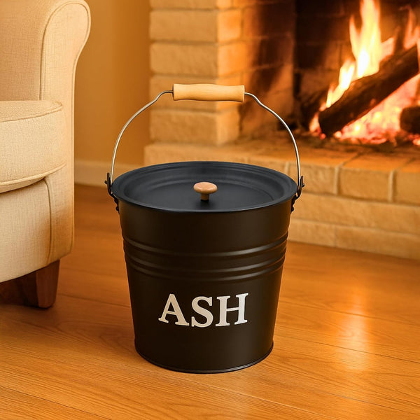 Black metal ash bucket with 'ASH' text in front of a fireplace.