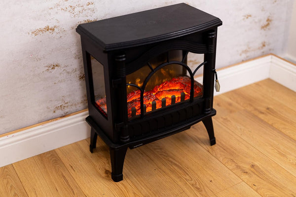 Black electric stove with flame effect on a wooden floor against a wall.