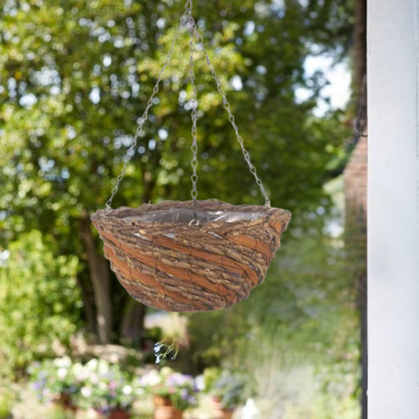 Hanging terracotta planter in a garden setting with trees and plants in the background