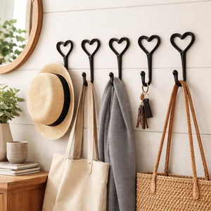 Heart-shaped hooks on a wall with bags, hats, and scarves hanging from them.