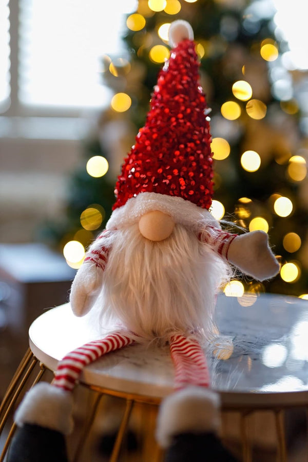 Decorative gnome with a red hat on a stool in front of a Christmas tree.