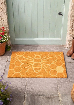 Orange doormat with bee design in front of a green door.