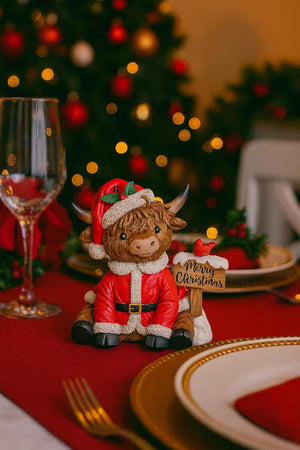 Cow figurine in Santa outfit on a Christmas-themed table with decorations and lights.