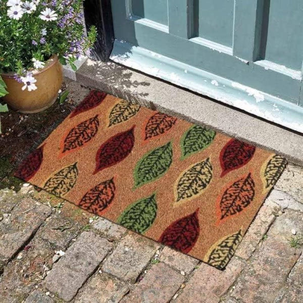 Doormat with leaf pattern on a brick pathway in front of a door.