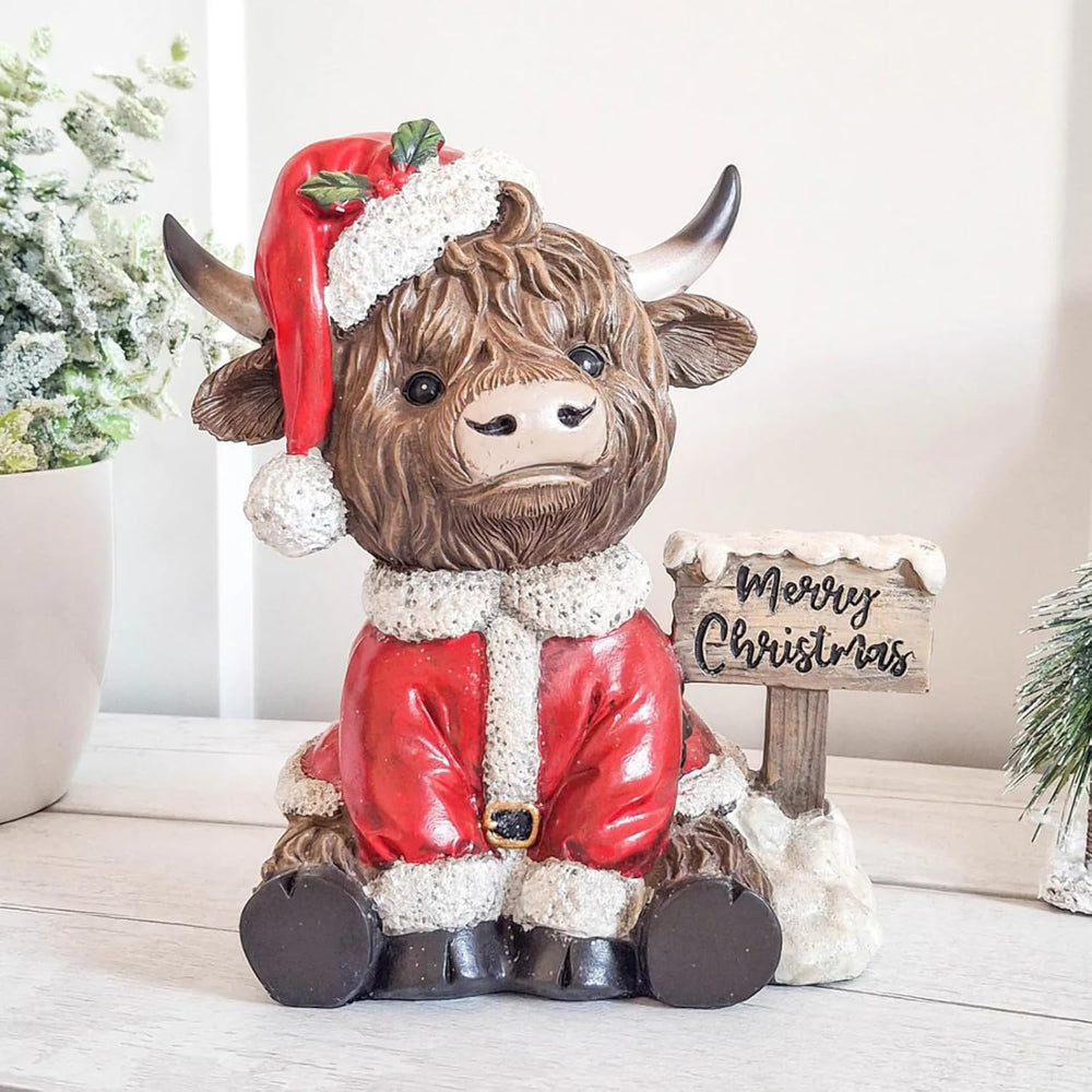 Cow figurine in a Santa outfit with a 'Merry Christmas' sign against a festive background.