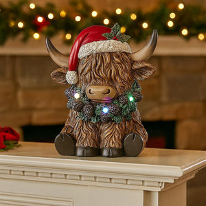 Decorative Highland cow figurine wearing a Santa hat with lights on a mantelpiece.