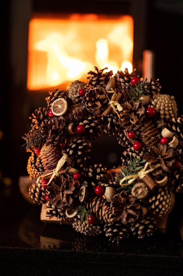 Decorative pine cone wreath with red berries in front of a fireplace.