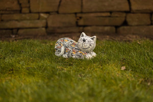 Decorative stone cat figurine on grass with a stone wall background