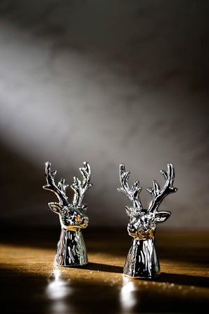 Two silver deer salt and pepper shakers on a reflective surface with a dark background