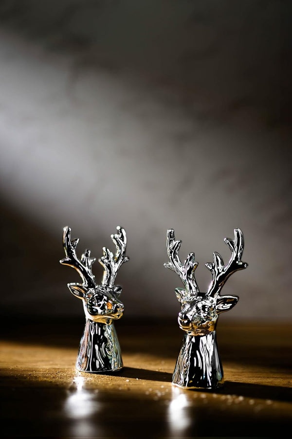 Two silver deer salt and pepper shakers on a reflective surface with a dark background