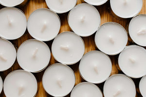 Multiple small white candles arranged closely together on a wooden surface.