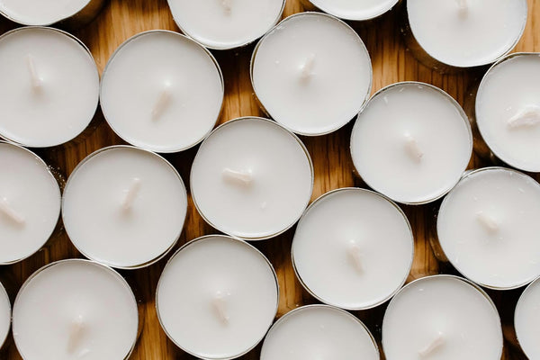 Multiple small white candles arranged closely together on a wooden surface.