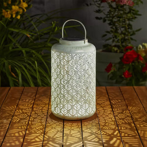 Decorative lantern with geometric pattern on a wooden surface with plants in the background