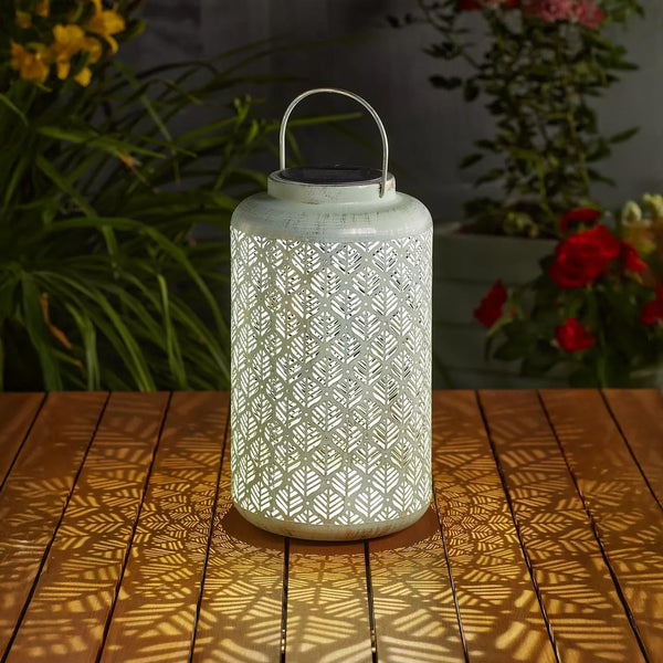 Decorative lantern with geometric pattern on a wooden surface with plants in the background