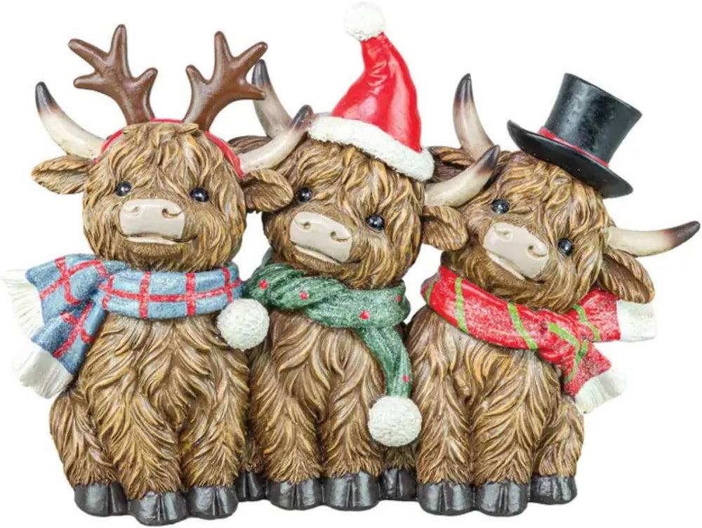 Three decorative Highland cow figurines wearing Christmas hats and scarves on a wooden surface.