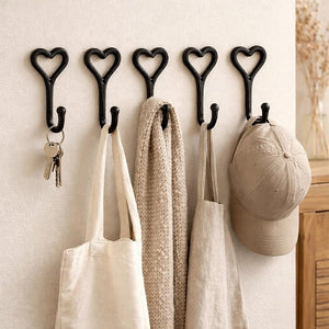 Heart-shaped hooks on a wall with bags, keys, and a cap hanging from them.