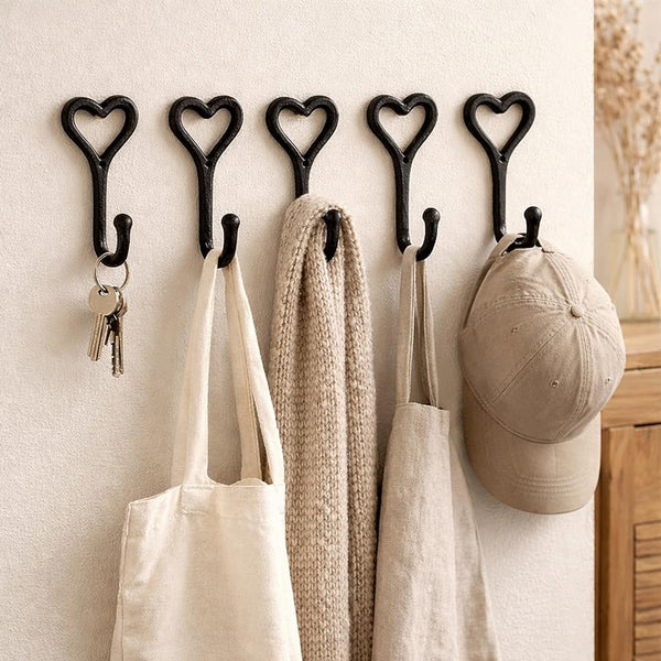 Heart-shaped hooks on a wall with bags, keys, and a cap hanging from them.