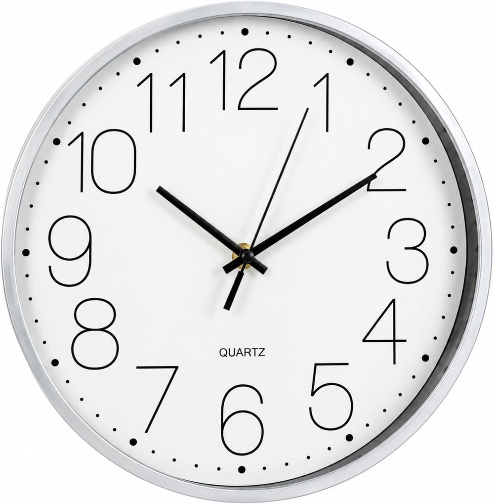 A round wall clock with a white face, black numerals and hands, and a silver-toned outer rim, mounted on a light beige wall in a bright kitchen setting.