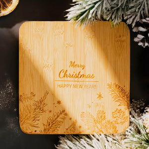 Wooden cutting board with 'Merry Christmas' and 'Happy New Year!' engraving, surrounded by festive decorations.