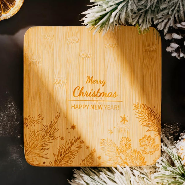 Wooden cutting board with 'Merry Christmas' and 'Happy New Year!' engraving, surrounded by festive decorations.