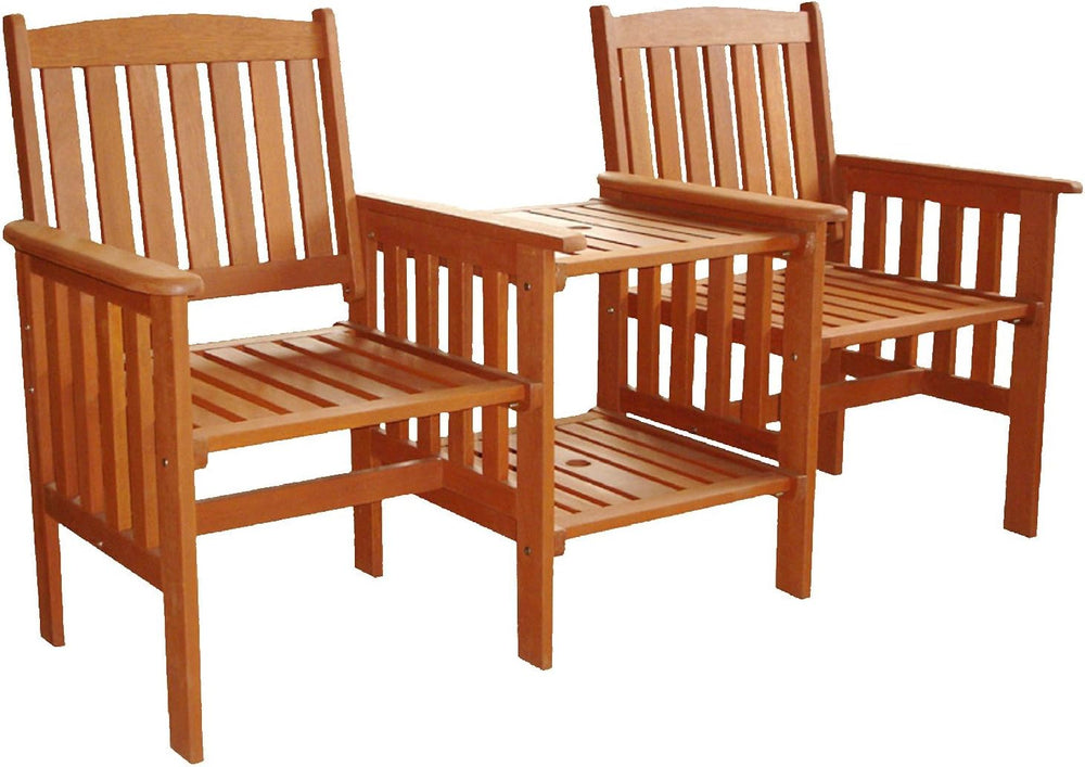 Two wooden chairs with a small table on a stone patio surrounded by greenery.