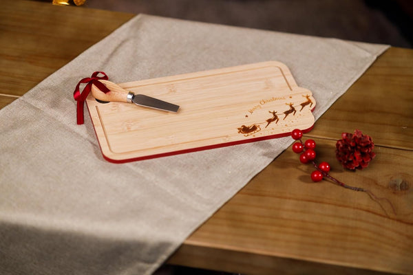 Wooden cutting board with engraved designs on a wooden table with a red ribbon and knife.