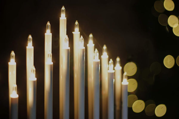 Row of lit candles against a dark background with blurred lights