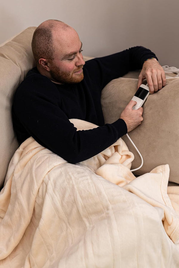 Man lying on a couch with a blanket, holding a remote control.