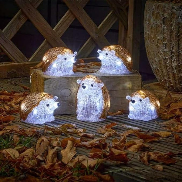 Decorative hedgehog lights on a wooden surface with leaves