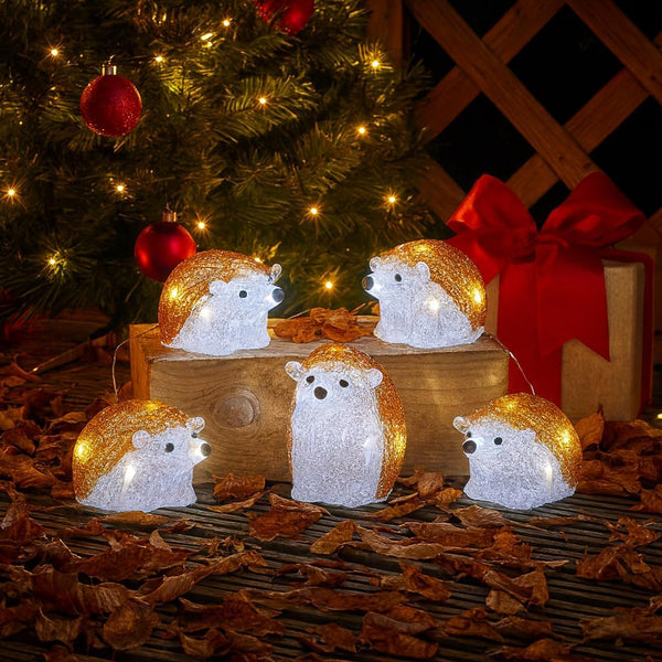 Decorative hedgehog lights on a wooden stand with a Christmas tree and gift in the background.