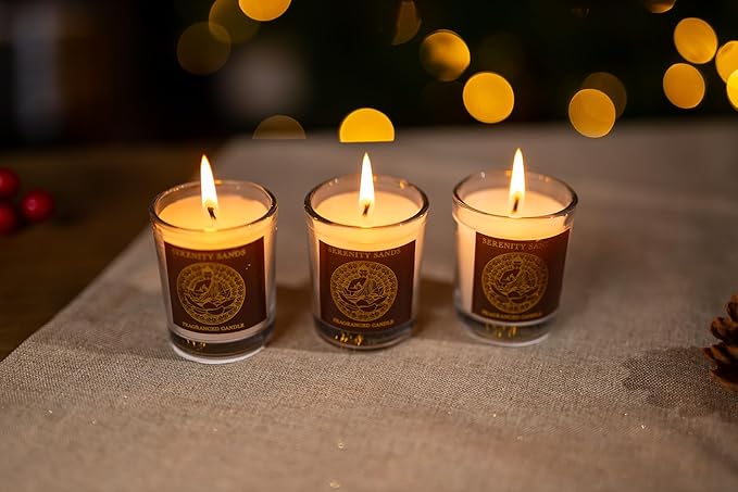 Three lit candles with labels on a textured surface with blurred lights in the background