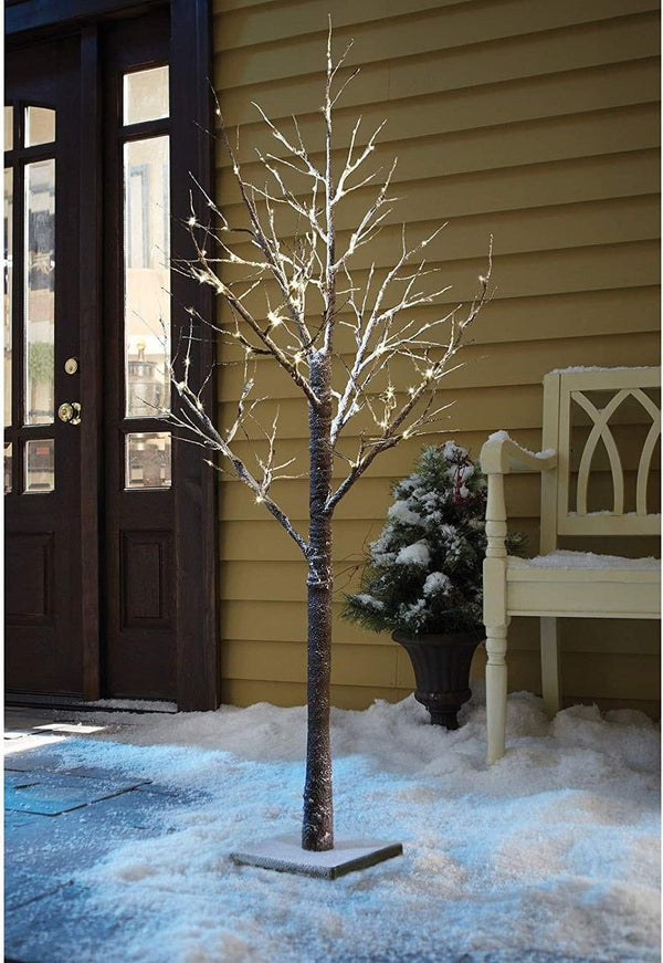Decorative lighted tree on a snowy porch with a bench and door in the background.