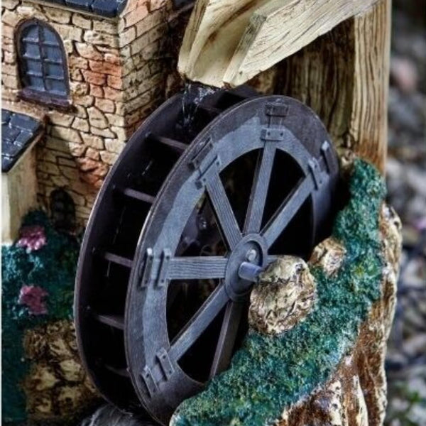A miniature decorative water wheel structure with a stone-textured building, wooden beam, mossy base, and small rocks, shown in close-up.