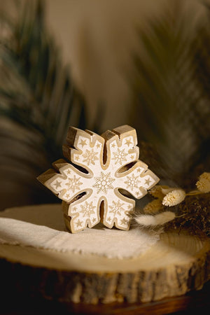 Decorative wooden snowflake ornament on a natural wood surface with blurred greenery in the background
