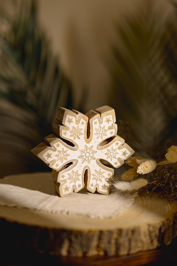 Decorative wooden snowflake ornament on a natural wood surface with blurred greenery in the background