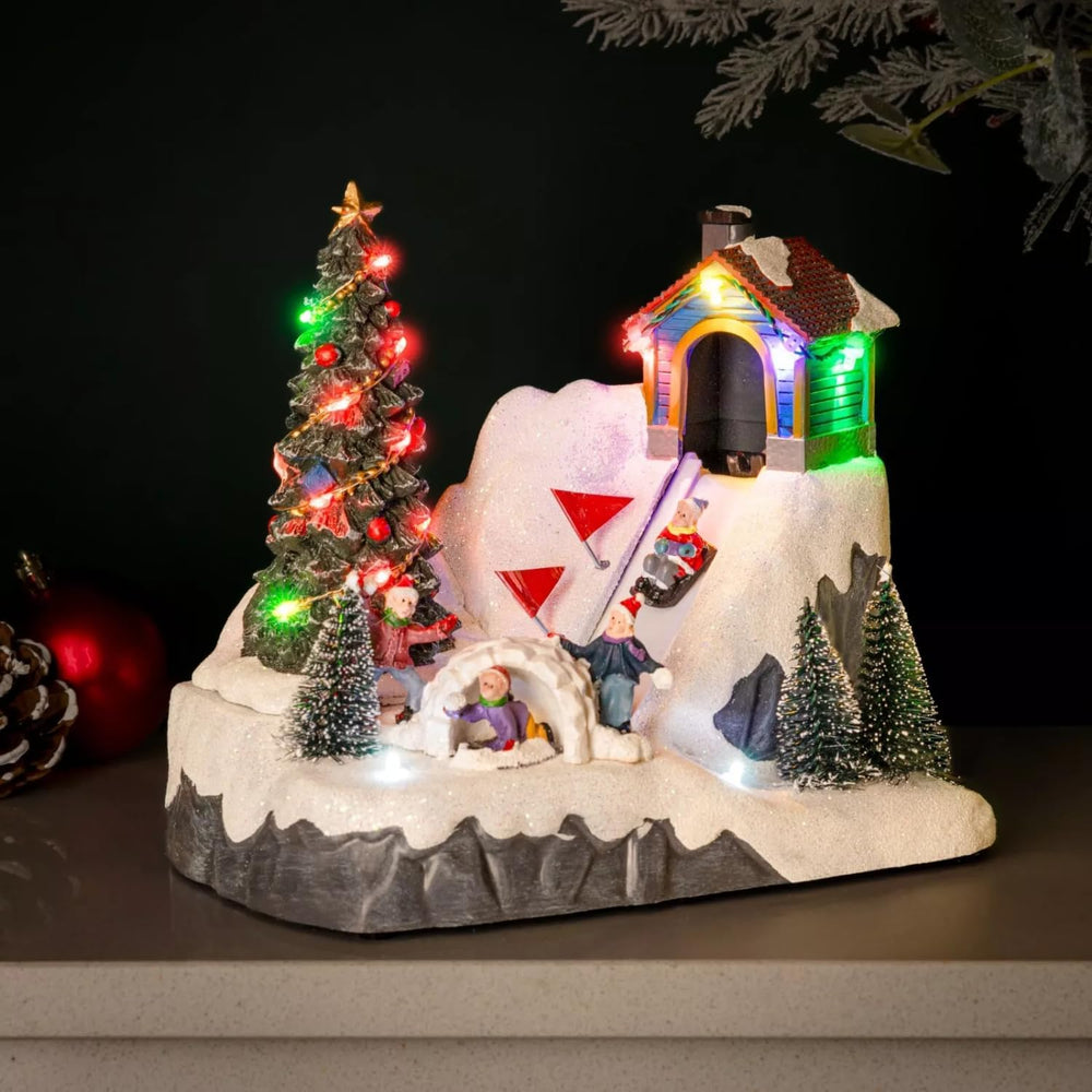 Christmas-themed diorama with a snow-covered igloo, Christmas tree, and small figures on a grey flat surface with a dark blurred background