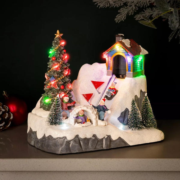 Christmas-themed diorama with a snow-covered igloo, Christmas tree, and small figures on a grey flat surface with a dark blurred background