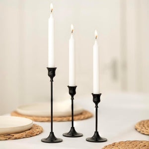 Three black candlesticks with white candles on a neutral background