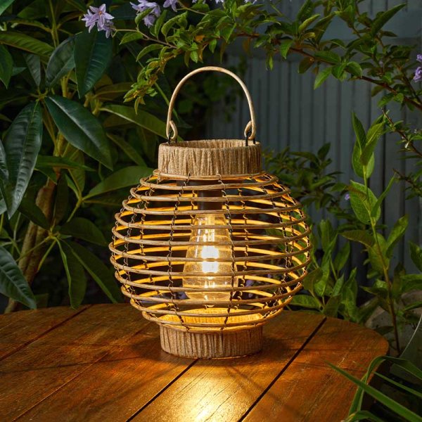 Wicker lantern on a wooden surface with plants in the background