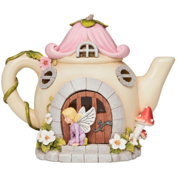 A whimsical fairy house teapot figurine with a pink roof, stone-textured base, a small blonde fairy kneeling at the door, and decorative mushrooms and flowers.