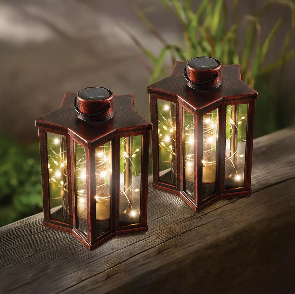 Two bronze effect star-shaped solar garden lanterns with firefly lighting effect, placed on a wooden surface outdoors.