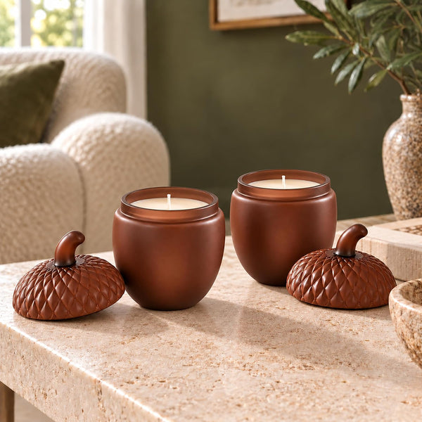 Three brown ceramic candle jars with matching acorn-shaped lids sit on a stone table in a cozy living room setting.
