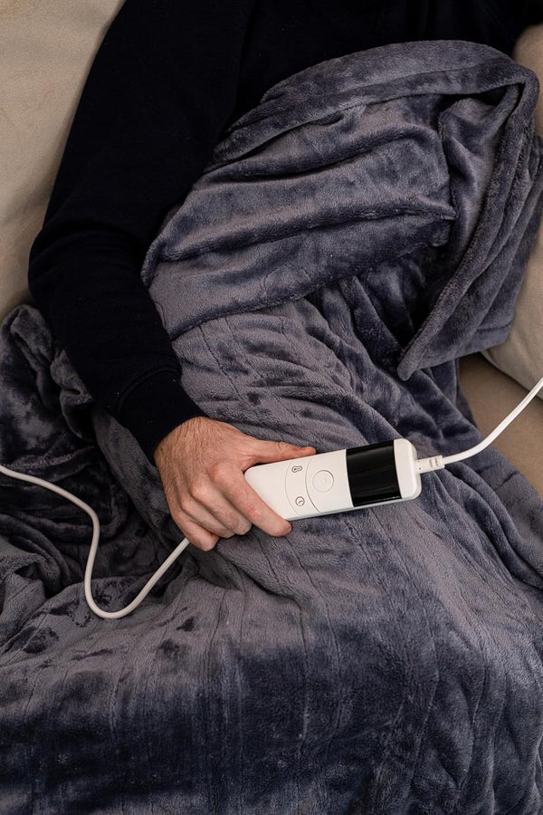 Person holding a white electronic device on a gray blanket