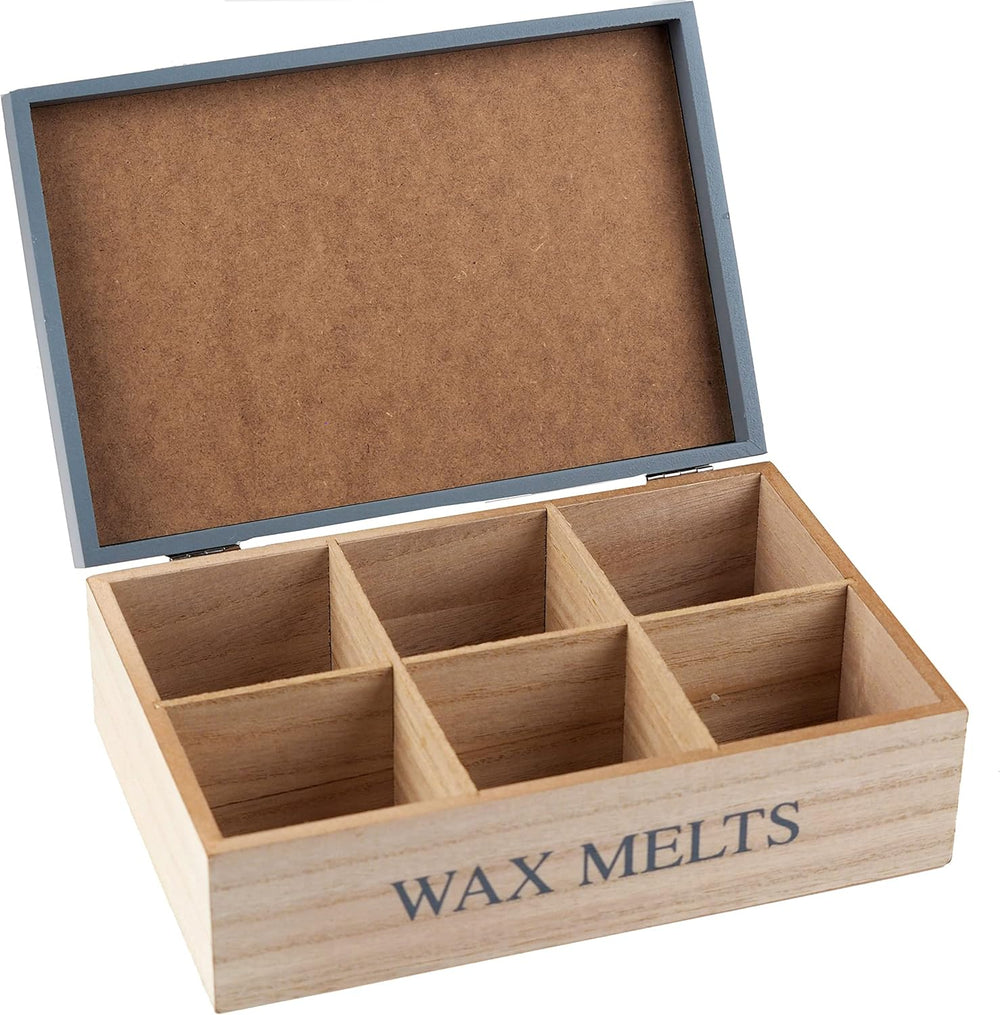Wooden box of wax melts with colorful wax melts inside, on a table with a candle in the background.